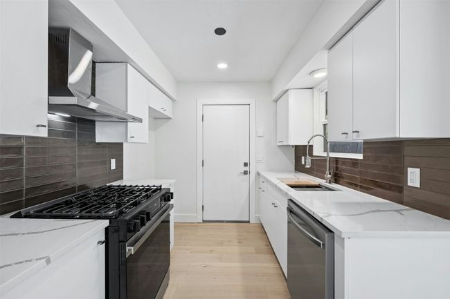 Kitchen with black range with gas cooktop, dishwasher, wall chimney range hood, light stone counters, and recessed lighting | Image 14