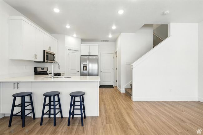 Kitchen featuring stainless steel appliances, light wood-type flooring, a peninsula, a kitchen bar, and recessed lighting | Image 4