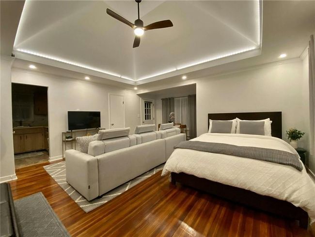 Bedroom area with a tray ceiling with ceiling fan, hardwood flooring, adjoining bathroom and walk-in closet | Image 38