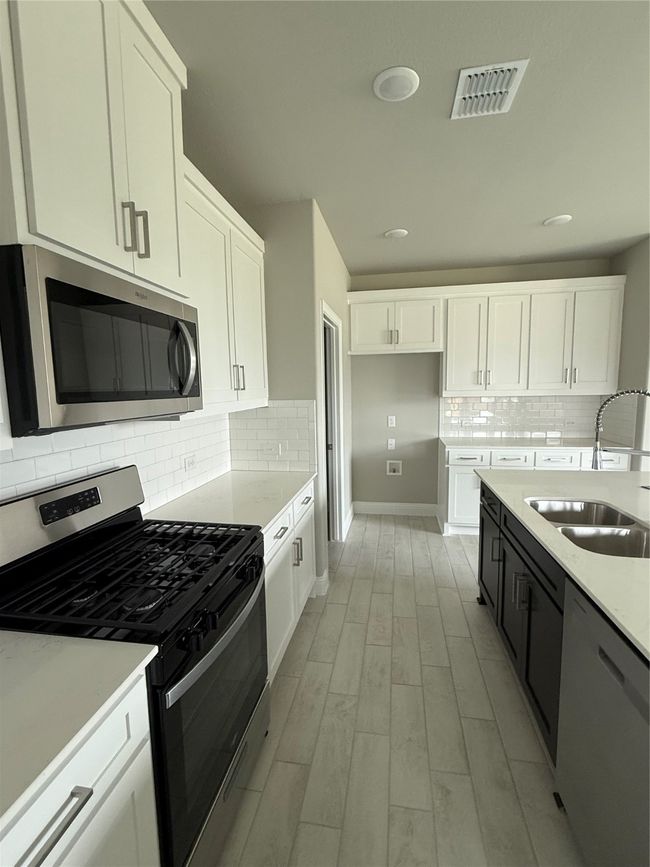 Kitchen with range, dishwasher, light wood-type flooring, white cabinets, and decorative backsplash | Image 7