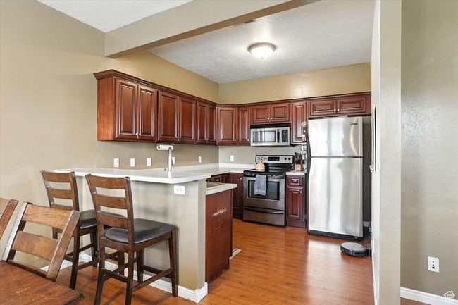 Kitchen with stainless steel appliances, a peninsula, light wood-style floors, a kitchen bar, and light countertops | Image 8