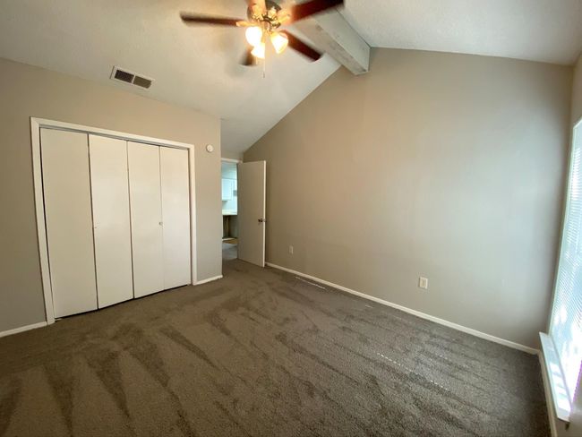 Unfurnished bedroom featuring ceiling fan, lofted ceiling with beams, a closet, and dark colored carpet | Image 5