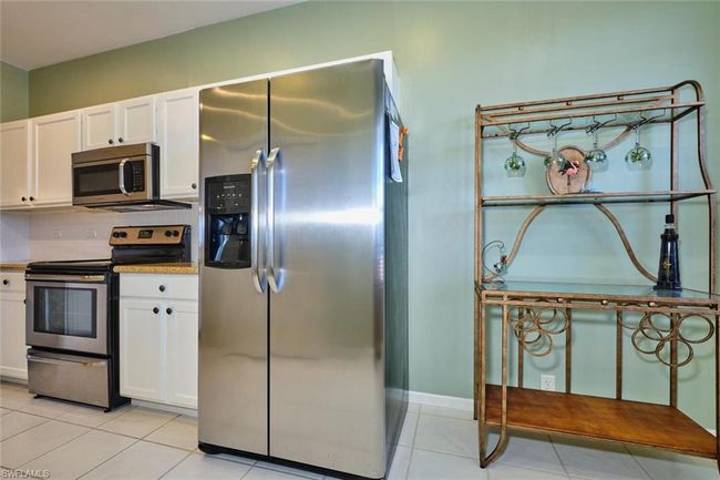 Kitchen with light tile patterned floors, white cabinets, backsplash, and stainless steel appliances | Image 23