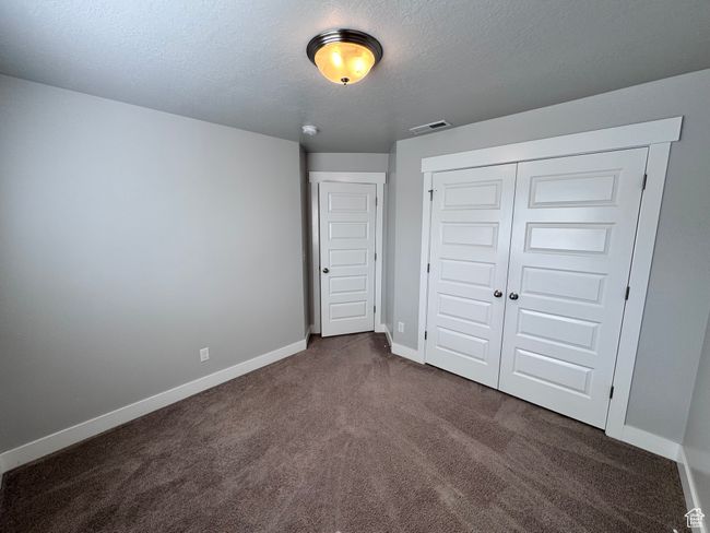 Unfurnished bedroom with dark carpet, a textured ceiling, a closet, and baseboards | Image 26