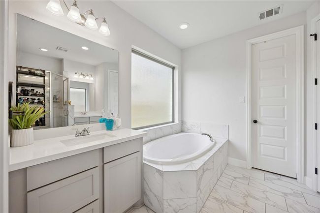 This bright bathroom features a luxurious soaking tub with marble accents, a large vanity with ample storage, and modern fixtures. A frosted window provides natural light while ensuring privacy. | Image 24