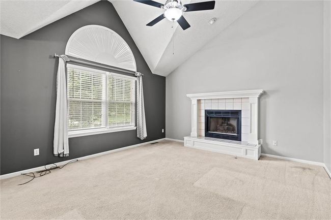 Unfurnished living room featuring lofted ceiling, ceiling fan, carpet flooring, a fireplace, and a textured ceiling | Image 6
