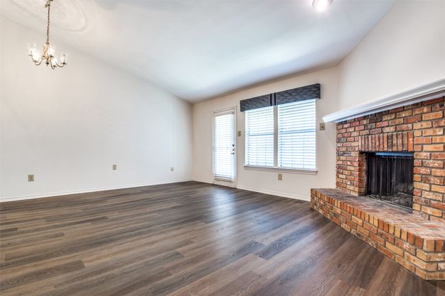 Unfurnished living room with a brick fireplace, a notable chandelier, dark hardwood / wood-style floors, and vaulted ceiling | Image 7