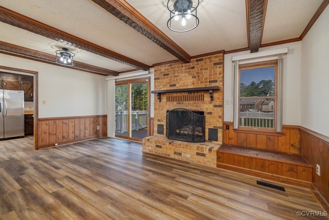 Unfurnished living room with a textured ceiling, wood walls, hardwood / wood-style floors, ornamental molding, and a brick fireplace | Image 4
