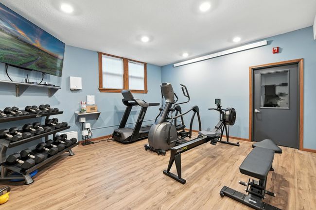 On-site workout facility with treadmills, rowing machine, weights, and wall-mounted TV for resident use. | Image 26
