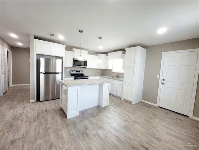 Kitchen with stainless steel appliances, recessed lighting, white cabinetry, light wood finished floors, and a kitchen island | Image 8