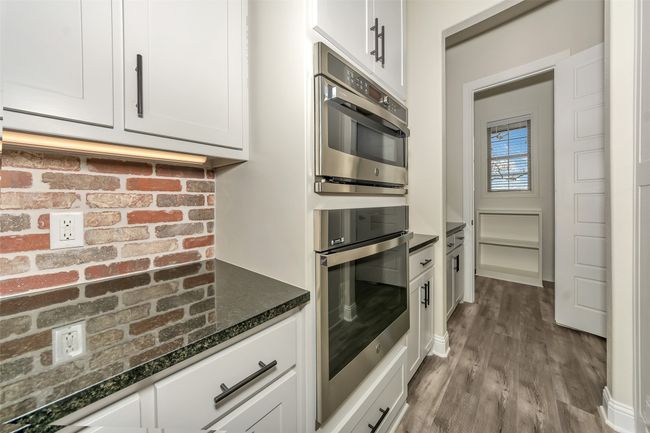 Kitchen with dark stone countertops, stainless steel double oven, white cabinets, and wood finished floors | Image 15