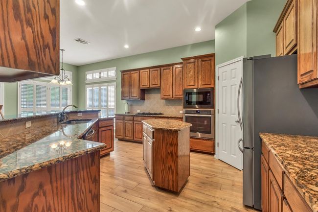 Kitchen with visible vents, a sink, a center island, brown cabinetry, and appliances with stainless steel finishes | Image 7