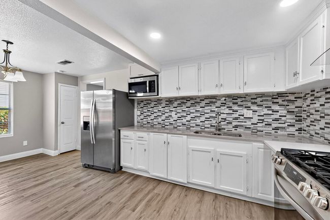 Kitchen featuring stainless steel appliances, light wood-style floors, white cabinetry, light countertops, and tasteful backsplash | Image 27