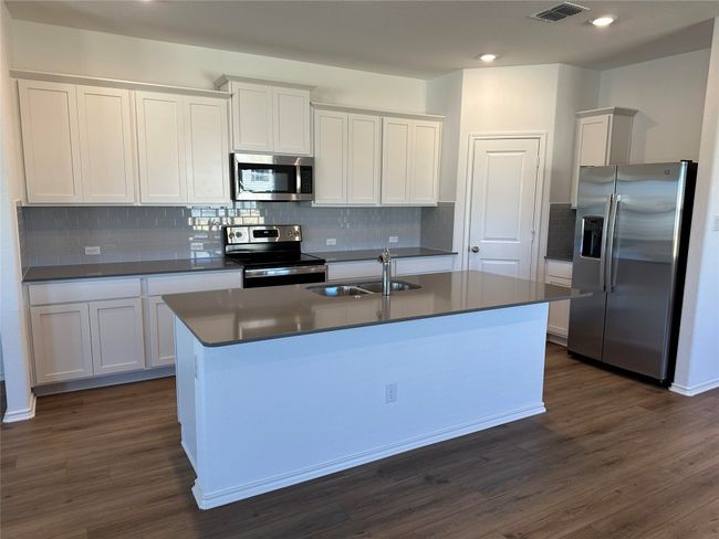 Kitchen featuring visible vents, appliances with stainless steel finishes, dark countertops, a sink, and an island with sink | Image 4