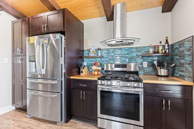 kitchen featuring open shelves, exhaust hood, beamed ceiling, decorative backsplash, and appliances with stainless steel finishes | Image 16