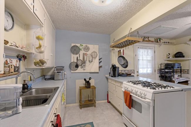 Kitchen featuring white cabinetry, sink, light tile patterned floors, white gas range oven, and a textured ceiling | Image 16