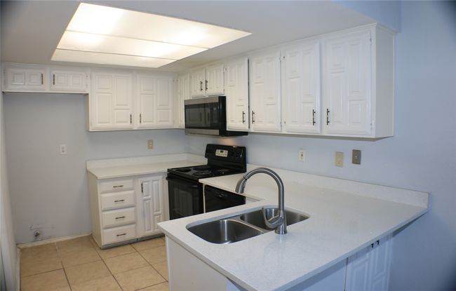 Kitchen featuring stainless steel microwave, black electric range, a peninsula, and white cabinetry | Image 17
