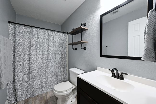 Full bath featuring wood finished floors, toilet, vanity, a textured wall, and curtained shower | Image 30