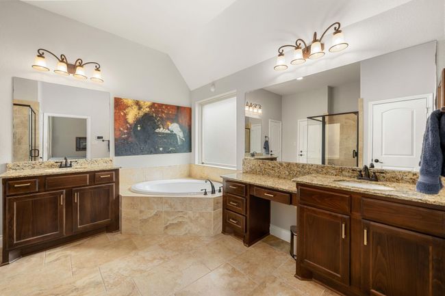 This primary bathroom is definitely move-in ready! Featuring a separate garden tub for soaking after a long day with custom tile detailing, dark stained cabinets with granite countertops, spacious walk-in closet with shelving, high ceilings, neutral paint, sleek and dark modern finishes. | Image 22