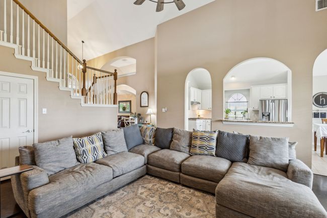 Living area with ceiling fan, arched walkways, high vaulted ceiling, and stairway | Image 9