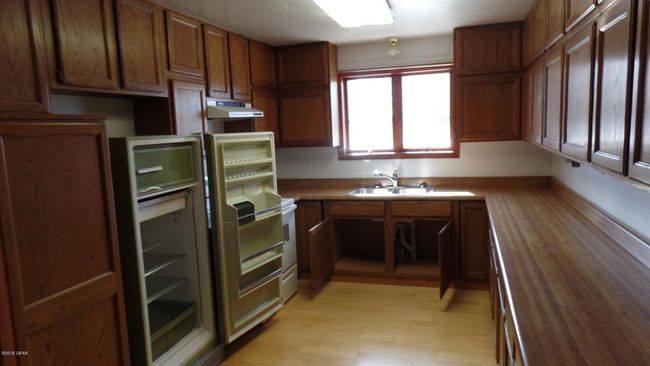 Kitchen with wood counters, light wood-style flooring, under cabinet range hood, brown cabinets, and a sink | Image 7