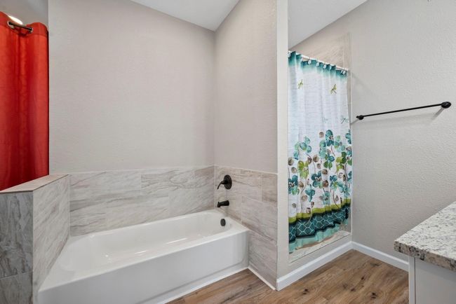Primary bath on first floor featuring wood finished floors, vanity, a bath, baseboards, and a shower with shower curtain | Image 6