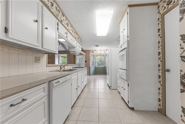 Kitchen featuring white appliances, a warming drawer, white cabinetry, tasteful backsplash, and a textured ceiling | Image 8