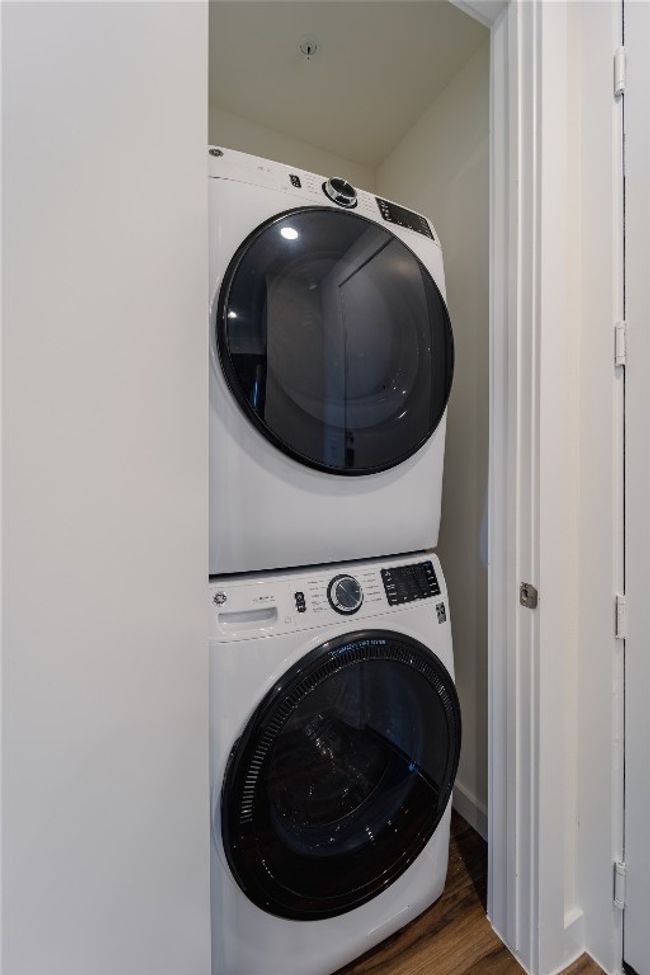 Laundry room with wood finished floors, stacked washer and clothes dryer, and laundry area | Image 7
