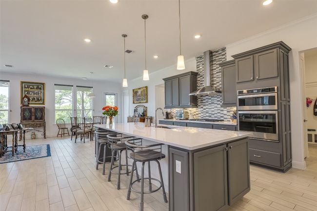 Kitchen with decorative light fixtures, backsplash, a breakfast bar, a kitchen island with sink, and light wood-style floors | Image 4