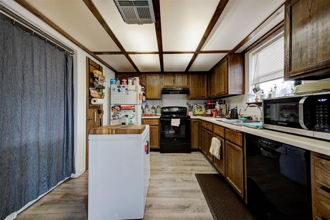 Kitchen featuring under cabinet range hood, light countertops, black appliances, a sink, and visible vents | Image 5