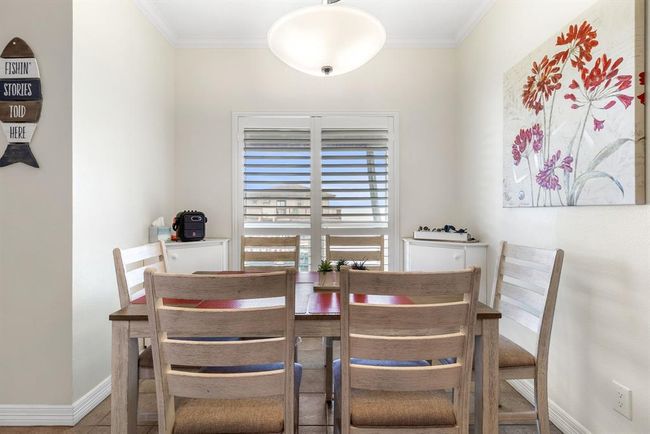 This cozy dining area features a wooden table with four chairs, bright natural light from shuttered windows, a modern light fixture, and tasteful wall art, offering a welcoming and intimate space. | Image 21