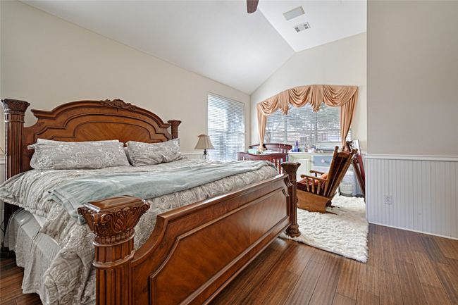 Bedroom with dark wood finished floors, lofted ceiling, visible vents, a ceiling fan, and wainscoting | Image 33