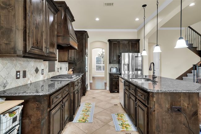 Kitchen featuring dark brown cabinets, tasteful backsplash, dark stone countertops, arched walkways, and decorative light fixtures | Image 5