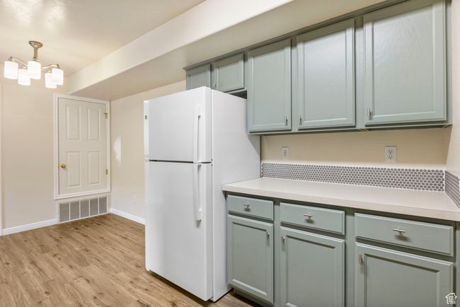 Kitchen with freestanding refrigerator, light countertops, light wood-style floors, baseboards, and a chandelier | Image 8