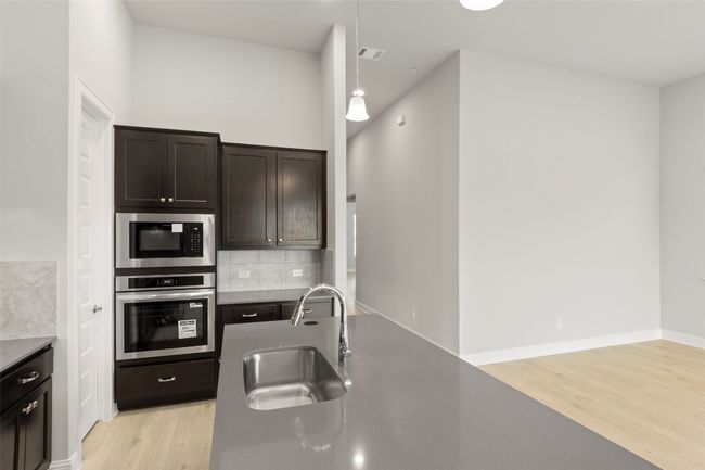 Kitchen with oven, light wood finished floors, built in microwave, backsplash, and dark brown cabinetry | Image 21