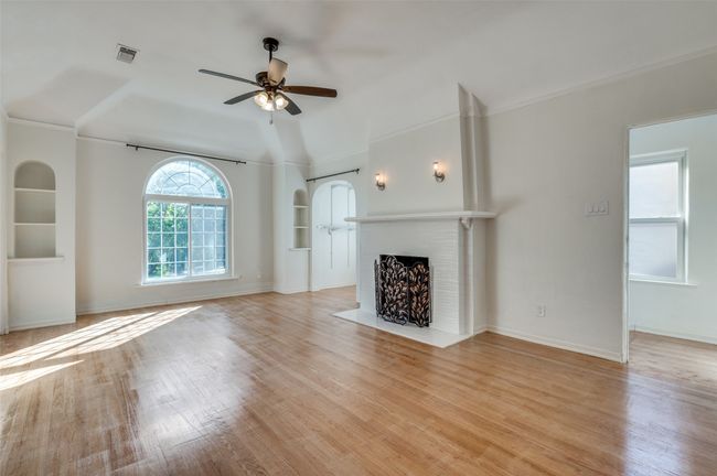 Unfurnished living room with a ceiling fan, crown molding, light wood-type flooring, a brick fireplace, and built in features | Image 20