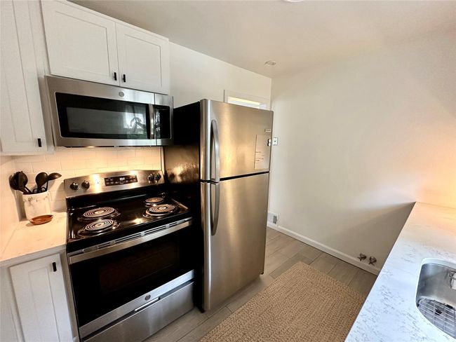 Kitchen featuring stainless steel appliances, tasteful backsplash, white cabinetry, light wood-type flooring, and baseboards | Image 10