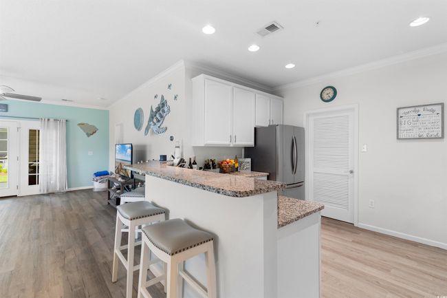 Kitchen featuring freestanding refrigerator, a breakfast bar area, ornamental molding, white cabinetry, and light wood finished floors | Image 8
