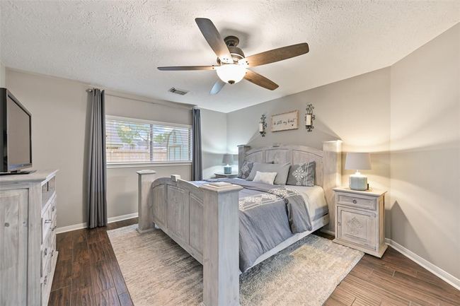 Escape to the peaceful primary suite with wood-look tile flooring, a neutral color palette, and a large window overlooking the backyard. A ceiling fan adds comfort to this serene retreat. | Image 11