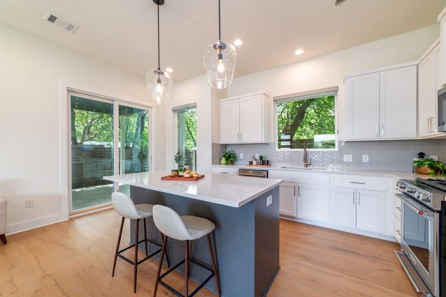 Kitchen with decorative backsplash, light countertops, high end stainless steel range, a kitchen island, and white cabinetry | Image 9
