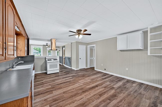 Kitchen featuring a ceiling fan, dark wood-type flooring, island exhaust hood, gas range gas stove, and ornamental molding | Image 11