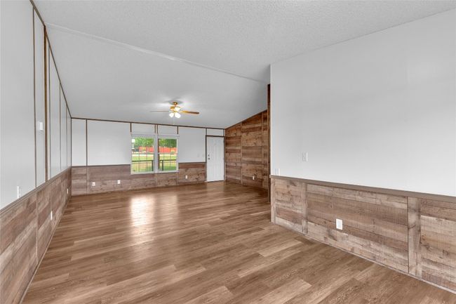Unfurnished room with wooden walls, a ceiling fan, wood finished floors, vaulted ceiling, and a wainscoted wall | Image 13