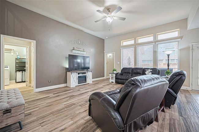 Step into the inviting living area, featuring three expansive floor-to-ceiling windows that overlook the backyard. Wood-look tile floors flow seamlessly throughout, complemented by a ceiling fan and a stylish accent wall that adds a subtle pop of color. | Image 18
