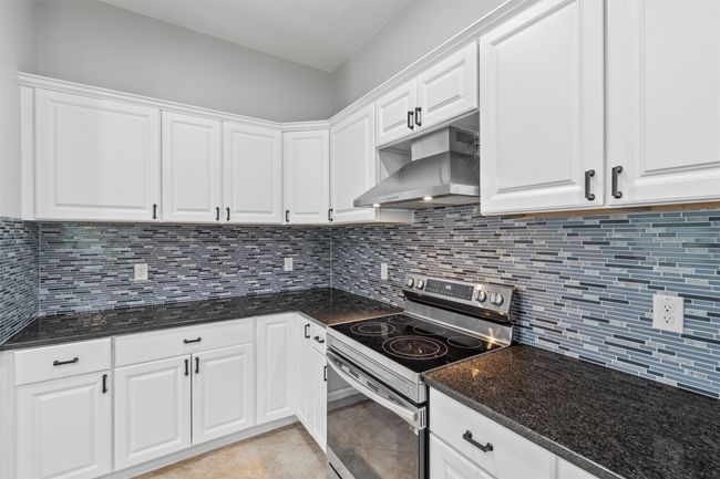 Kitchen featuring dark stone counters, stainless steel electric range oven, tasteful backsplash, light tile flooring, and white cabinetry | Image 11