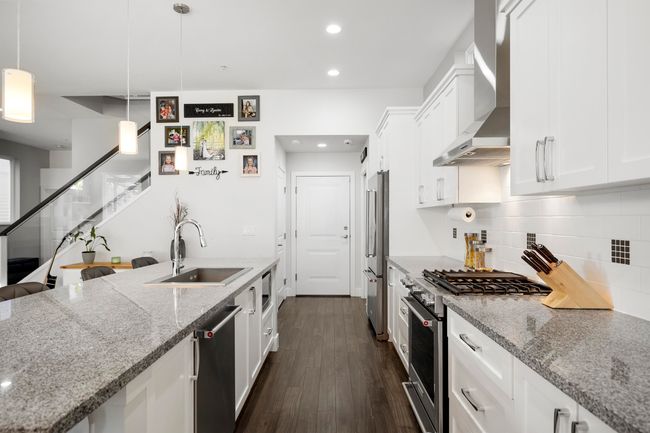 Kitchen featuring white cabinetry, high end appliances, wall chimney range hood, and a sink | Image 11
