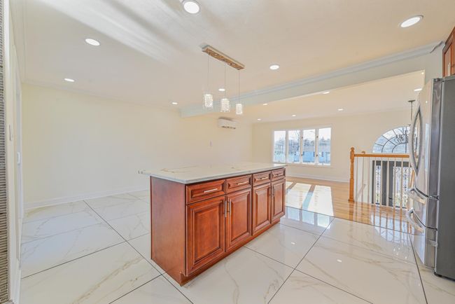Kitchen with crown molding, stainless steel fridge, hanging light fixtures, light stone counters, and a kitchen island | Image 22