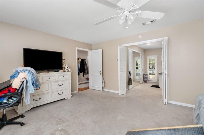 The primary bedroom features an en-suite area with a walk-in closet and additional space that can be used as a dressing area or sitting nook. Double doors open up to this versatile space, while another doorway provides easy access to the rest of the home. Neutral tones and soft carpeting create a cozy and inviting atmosphere. | Image 25