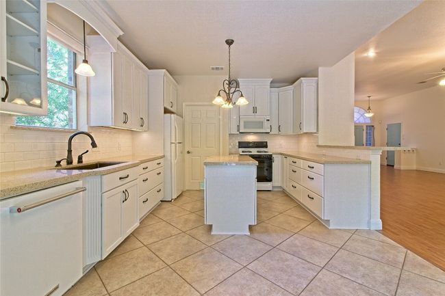 Kitchen with white appliances, a peninsula, backsplash, and white cabinetry | Image 18
