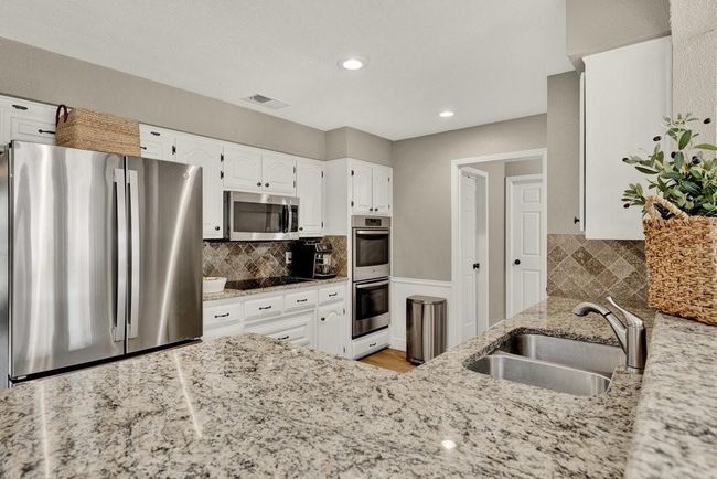 Kitchen with white cabinetry, stainless steel appliances, backsplash, a sink, and light stone countertops | Image 13