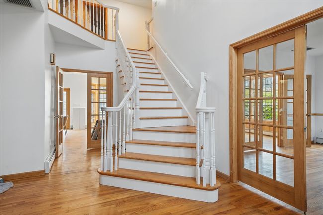 Staircase featuring french doors, visible vents, a towering ceiling, baseboards, and wood finished floors | Image 5